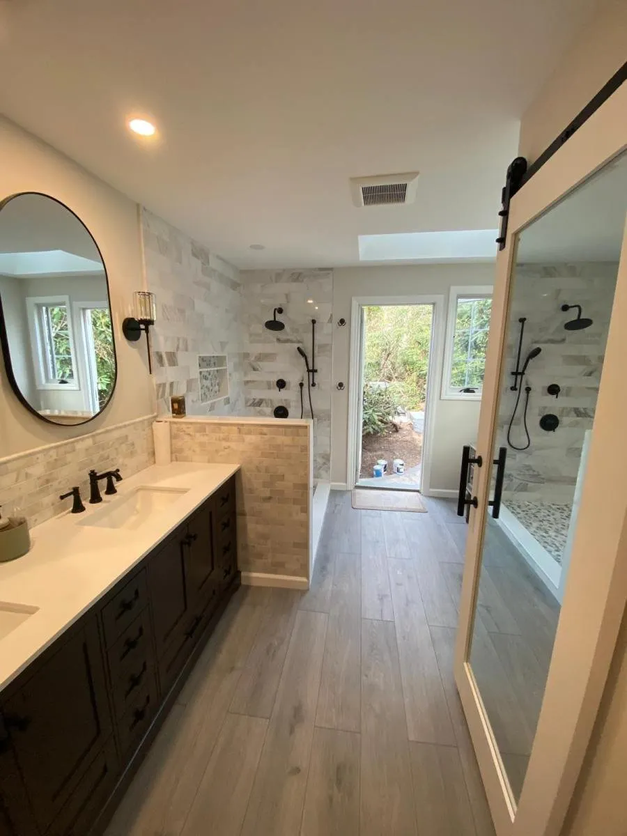 Renovated master bathroom with double vanity, round mirror and glass walk-in shower in Long Island, NY
