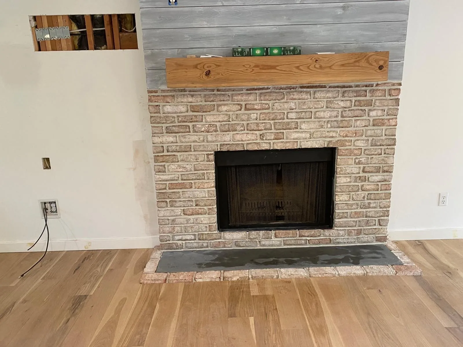 Chimenea de ladrillo blanqueado con repisa de madera recuperada y piso de madera